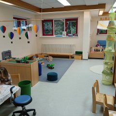 Im Gruppenraum gibt es einen großen Spielteppich und einen Tisch zum Basteln, An der Decke hängt ein großes Mobile