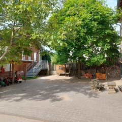 Blick in den Vorderhof des Kindergartens mit einem kleinen Unterstand für diverse Roller und andere Fahrzeuge und auf einen kleinen Sitzplatz