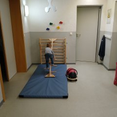 Rin Kind steht auf einer Turnmatte vor einer Sprossenwand
