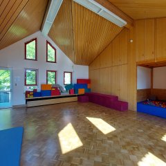 sonnendurchleuchteter Turnraum mit Holzboden, Turnmatten , diversen Spielgeräten und einem Ballbad