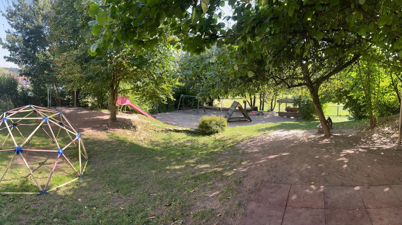 Garten im Kindergarten Purzelbär Blick in den Garten des Kindergartens Purzelbär mit Klettergerüst, Sandkasten, Schaukel und vielen Bäumen die Schatten spenden im Sommer